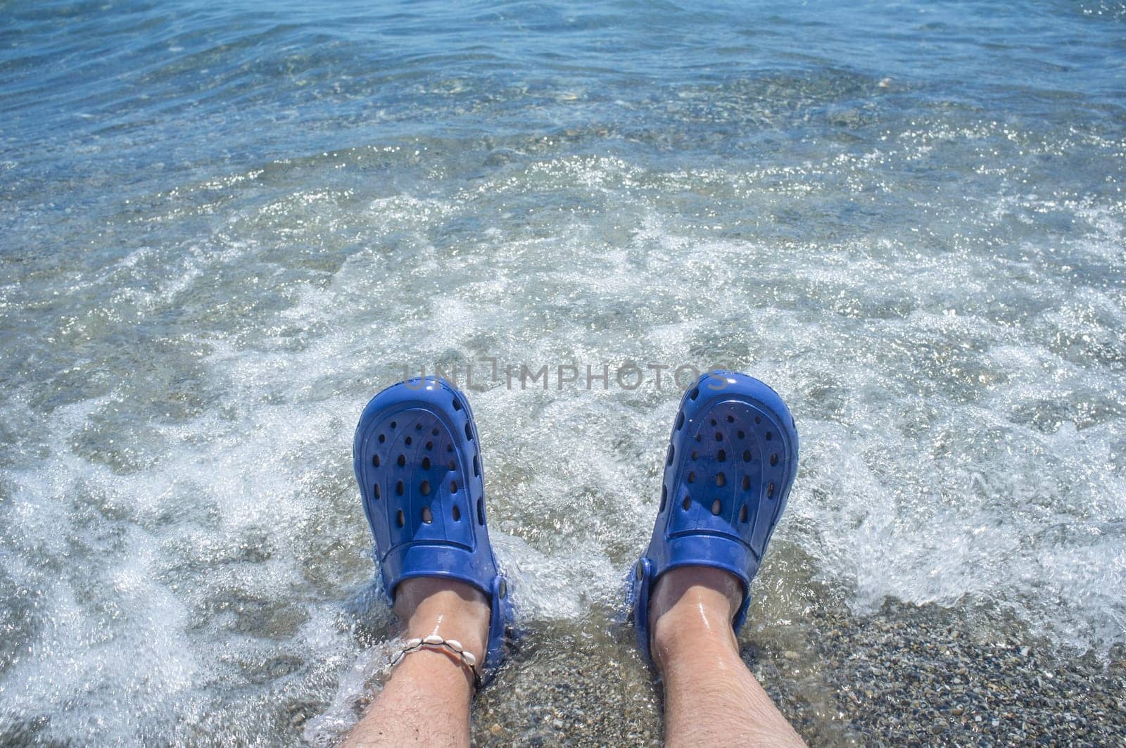 Male wearing blue clogs beside the beach. Selective focus