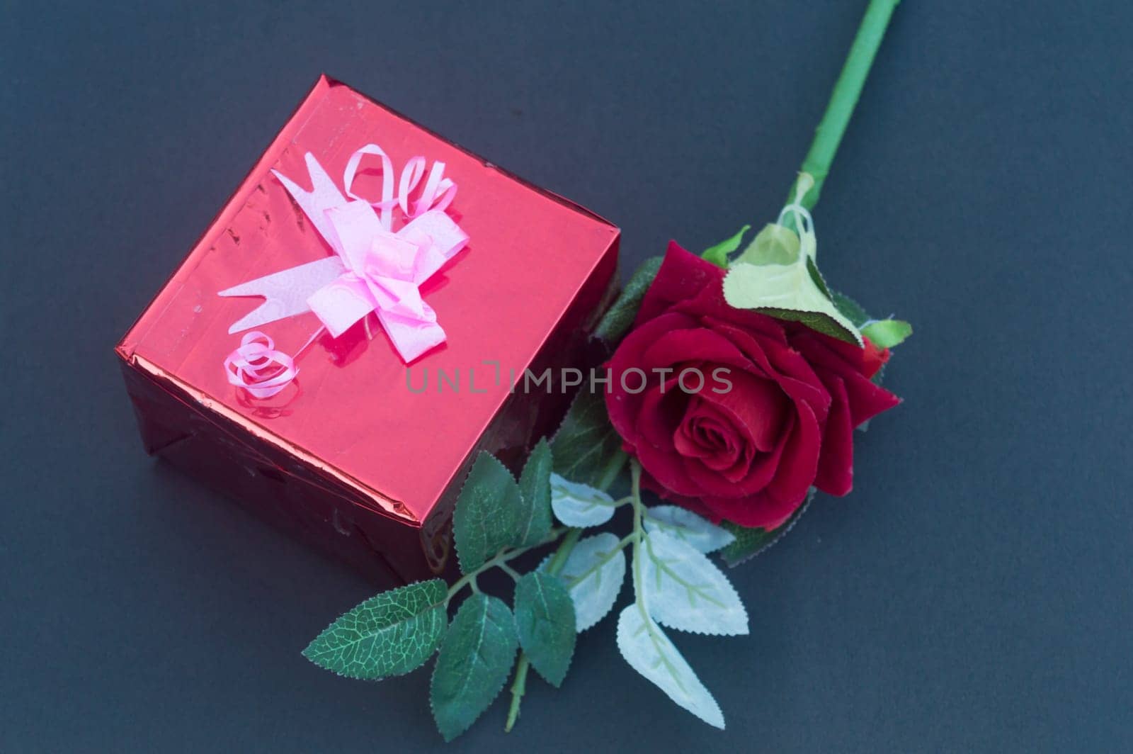 A red rose and a wrapped gift box with ribbon on table in blue background. High angle view. Flat Lay. Copy space room for text.
