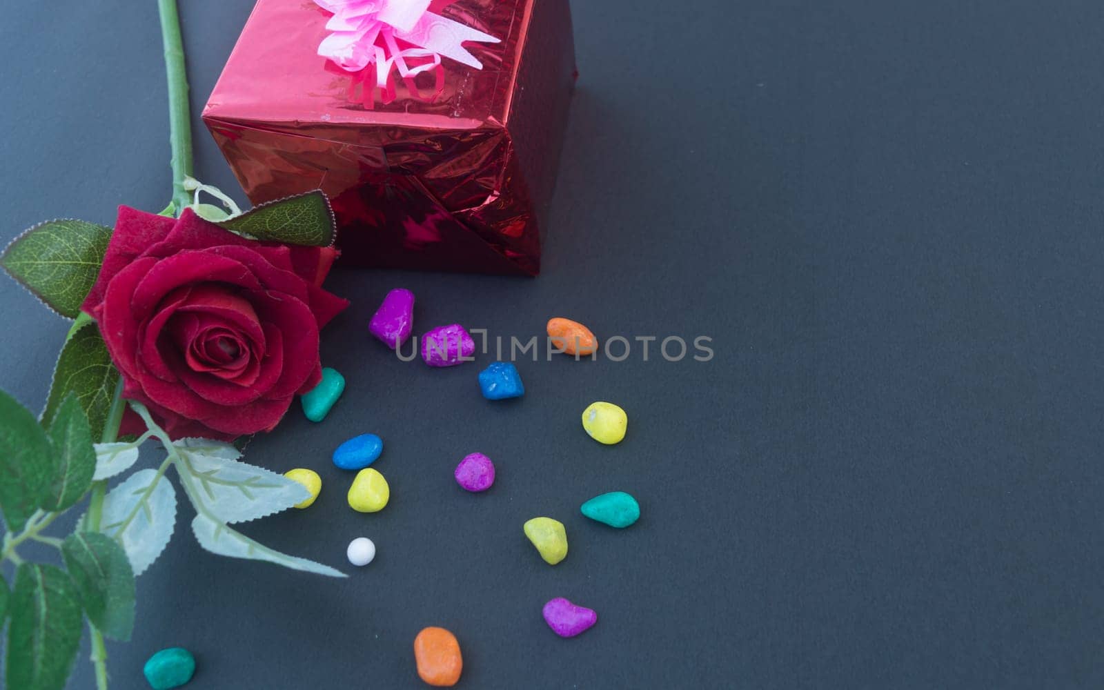 A red rose and a wrapped gift box with ribbon on table in blue background. High angle view. Flat Lay. Copy space room for text.