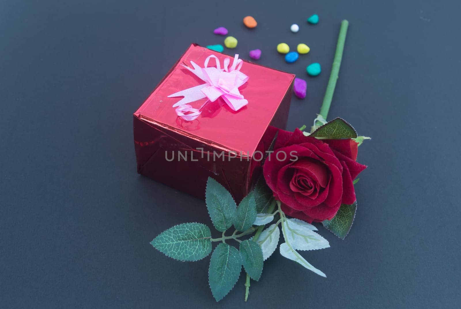 A red rose and a wrapped gift box with ribbon on table in blue background. High angle view. Flat Lay. Copy space room for text.