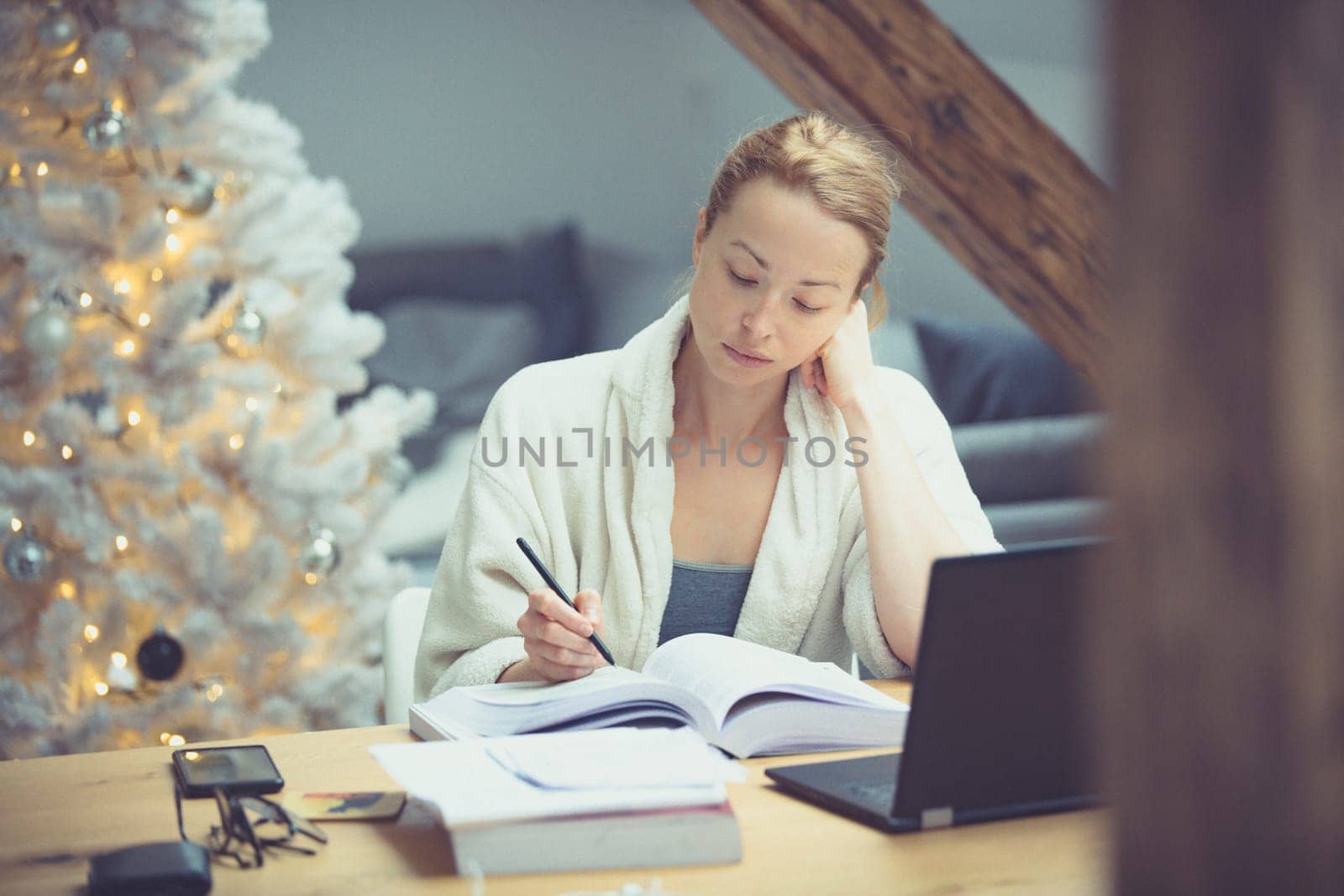 Young businesswoman wearing cosy warm bathrobe working remotly from home in winter Christmas time during 2020 corona virus pandemic. Work from home, selter in place, concept.