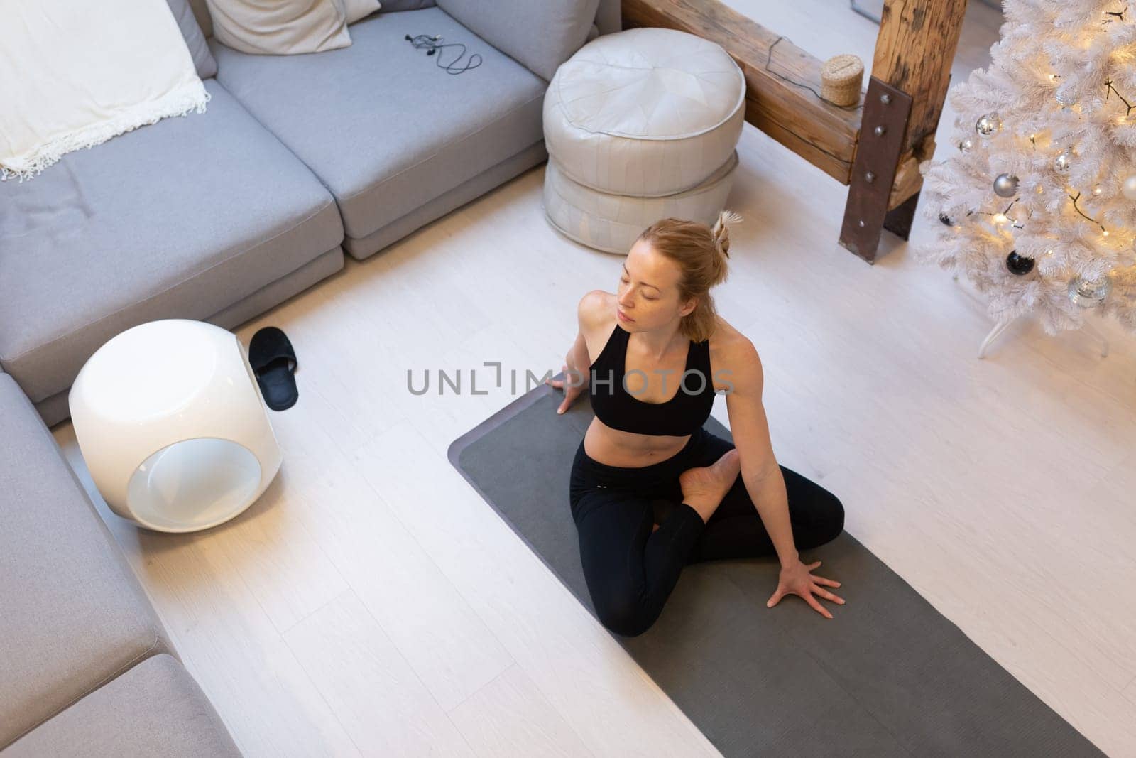 Beautiful blonde woman doing home workout indoors. Woman practice yoga at home. Fit girl using workout tutorials for healthy active lifestyle. Woman using quarantine for home workouts and stretching