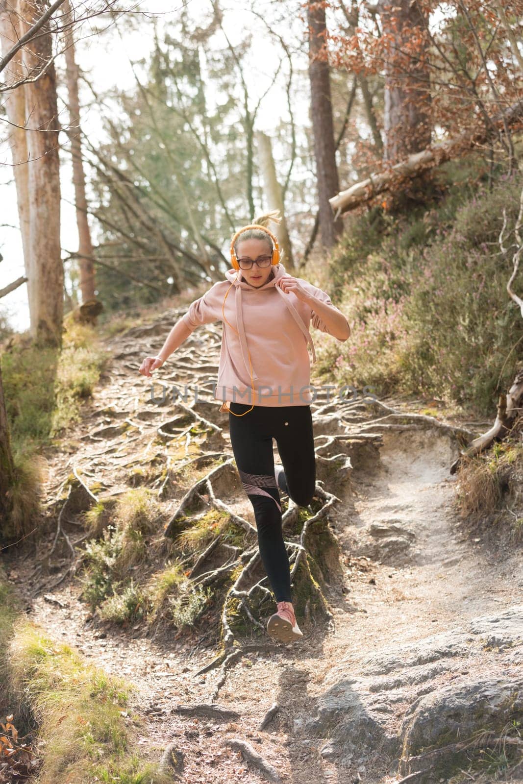 Active sporty woman running in autumn fall forest jumping over the roots on the path. Healthy lifestyle image of young active caucasian woman jogging outside in nature.