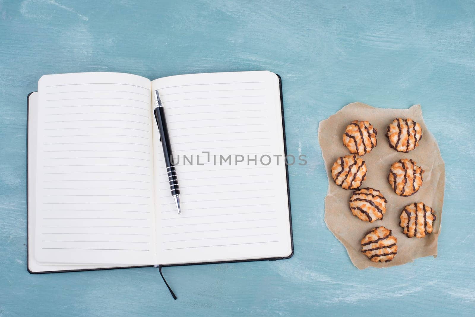 Coconut macaroons on a textured blue background, empty booklet with a pen