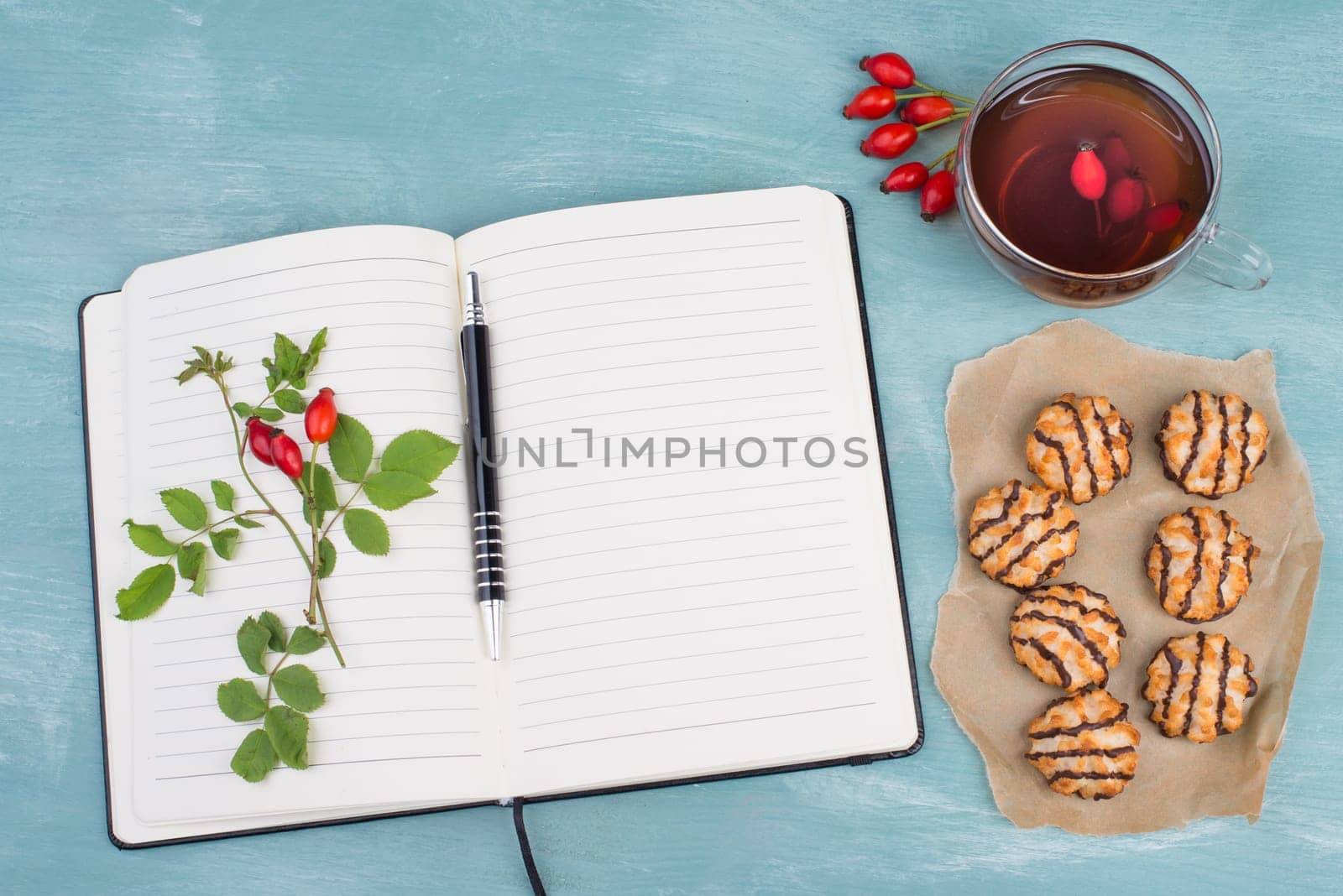 Coconut macaroons on a textured blue background, empty booklet with a pen, cup of tea