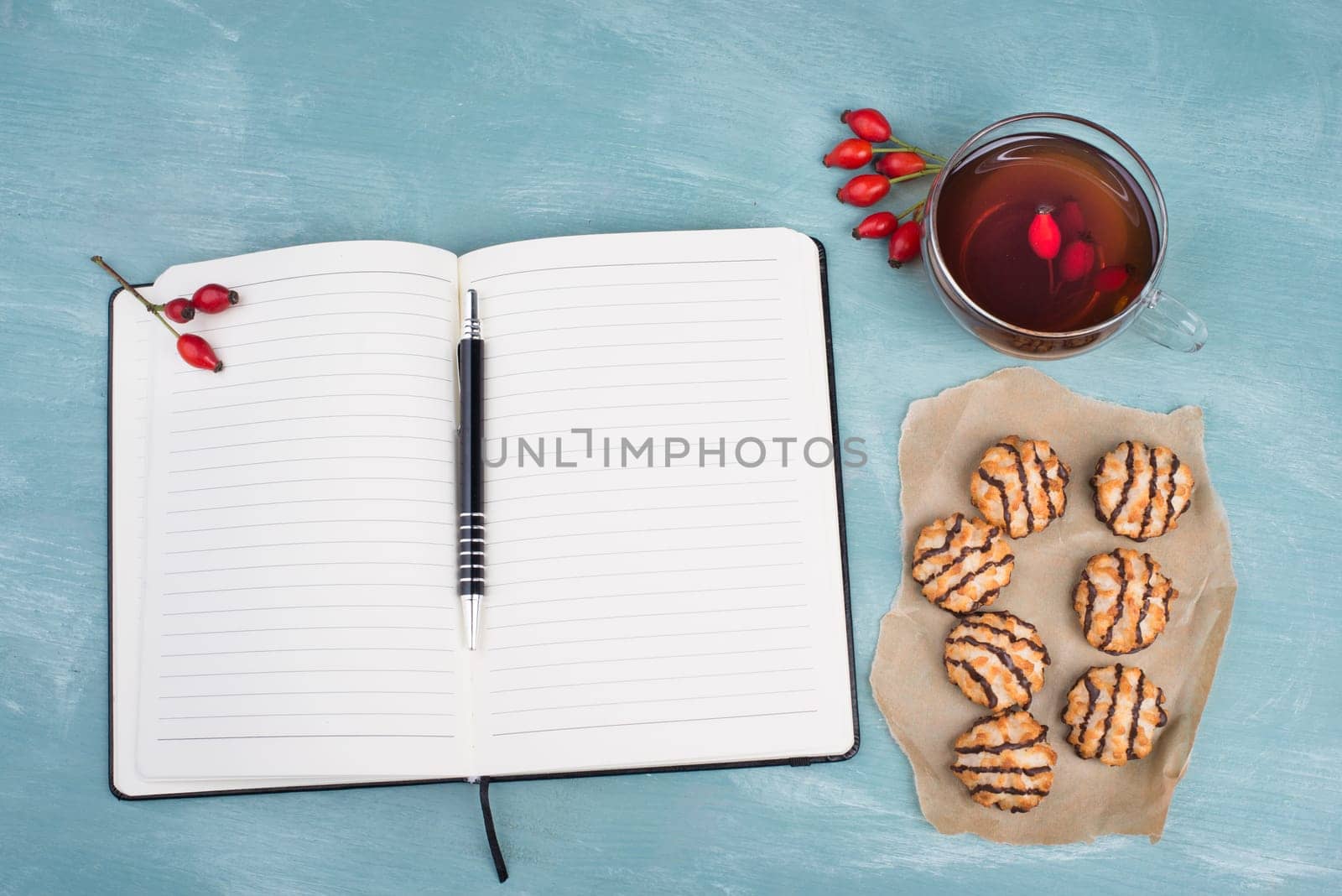 Coconut macaroons on a textured blue background, empty booklet with a pen, cup of tea