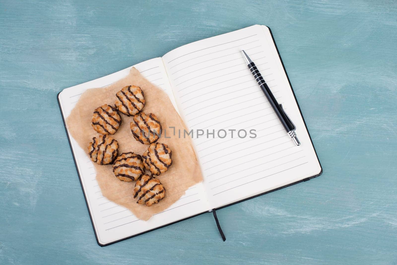 Coconut macaroons on a textured blue background, empty booklet with a pen