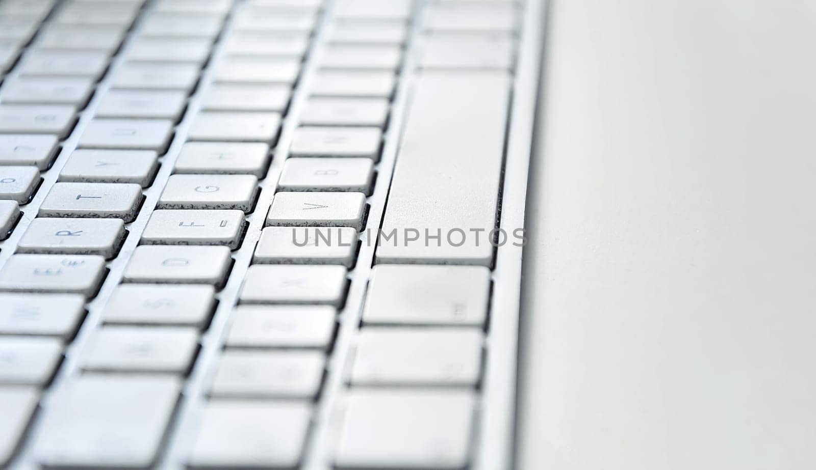 Detail of a modern white computer keyboard dirty and dusty on a white table. Computer hardware device. Technology and internet