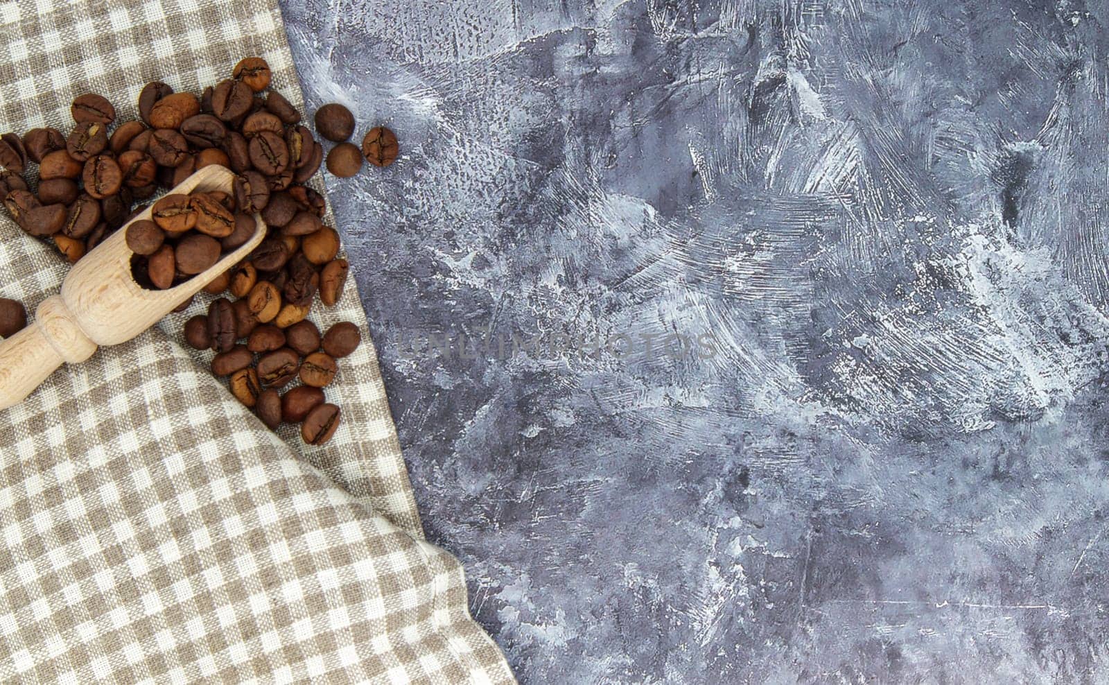 Roasted coffee beans on a stone gray textured table with a checkered textile handkerchief. Top view flat with copy space for your text