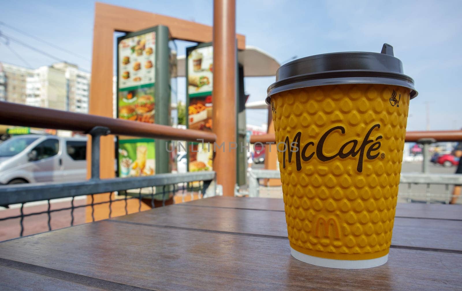 Paper yellow glass glass with coffee for McCafe drinks on the table against blurred city from McDonald's. Fast food business background. Fast food restaurant menu. Ukraine, Kiev - September 13, 2021