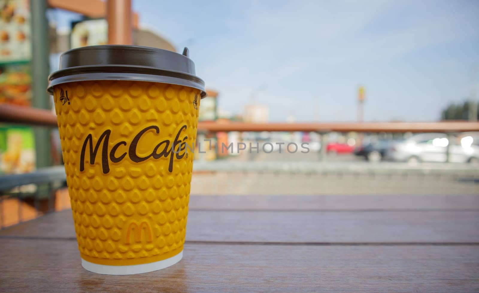 Paper yellow glass glass with coffee for McCafe drinks on the table against blurred city from McDonald's. Fast food business background. Fast food restaurant menu. Ukraine, Kiev - September 13, 2021