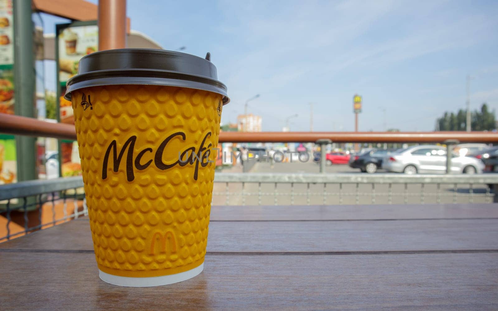 Paper yellow glass glass with coffee for McCafe drinks on the table against blurred city from McDonald's. Fast food business background. Fast food restaurant menu. Ukraine, Kiev - September 13, 2021