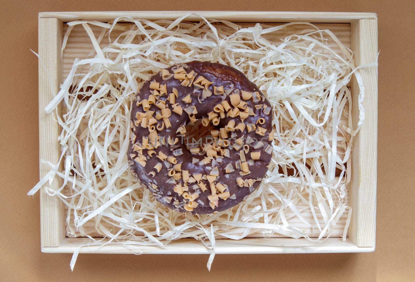 Fresh chocolate donut isolated on coffee background. Delicious dessert with glossy chocolate glaze. Sweet food concept with one round chocolate donut for your design and print. Top view, flat lay