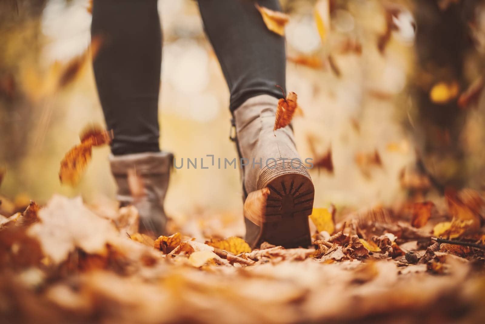 Woman walking alone in the autumnal park. Closeup view of the legs.