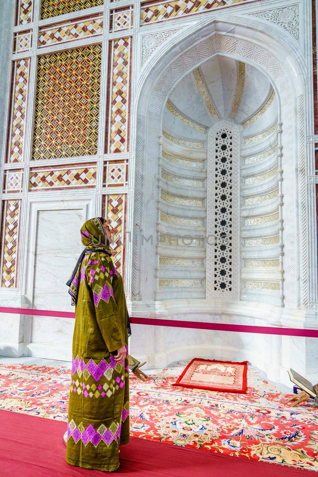 A woman dressed in a traditional omani abaya looking at an ornate alcove at the Muhammad al-Amin Mosque in Muscat, Oman