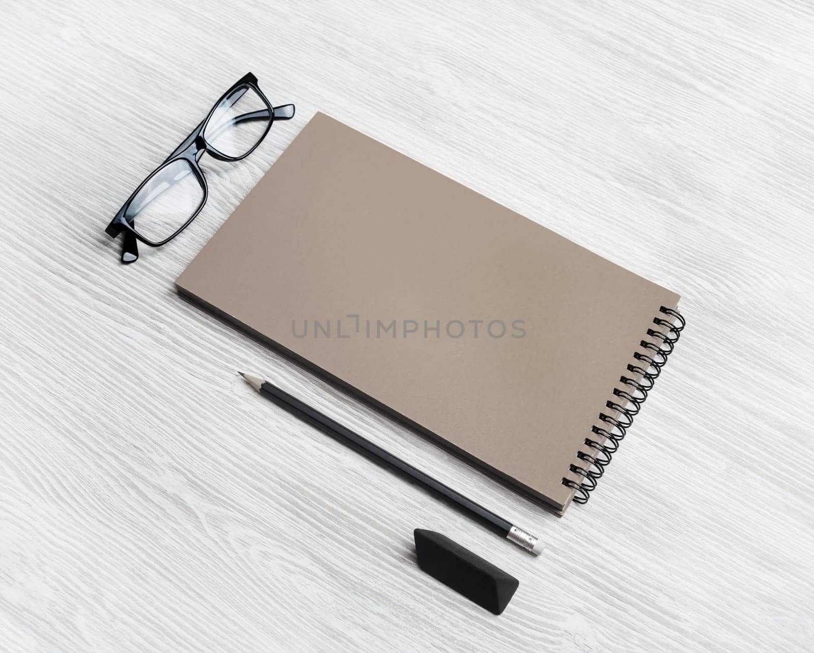Blank kraft sketchbook, glasses, pencil and eraser on light wood table background.