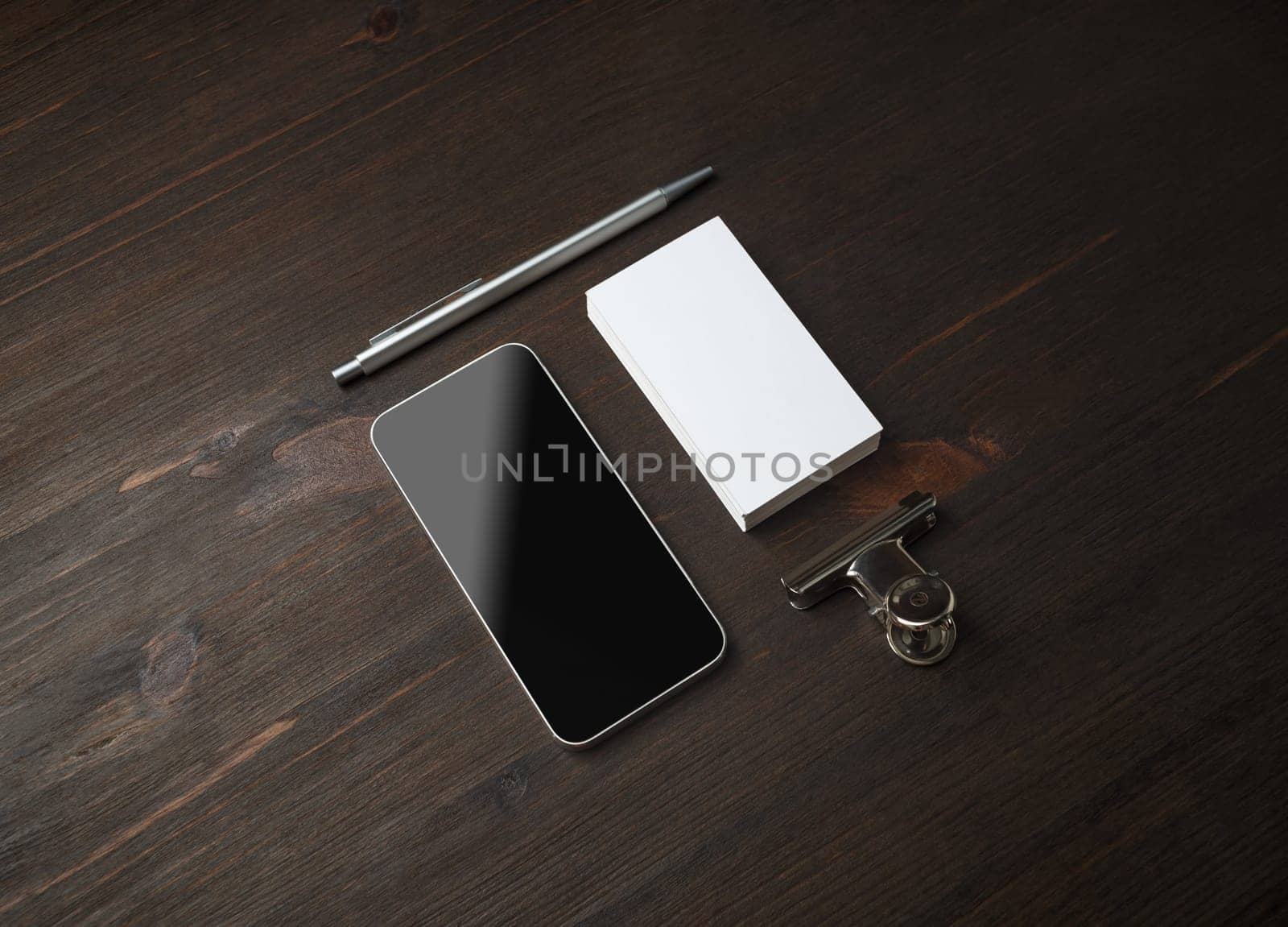 Smartphone and blank stationery: business card, pen and paper clip on wood table background. Template for branding identity.