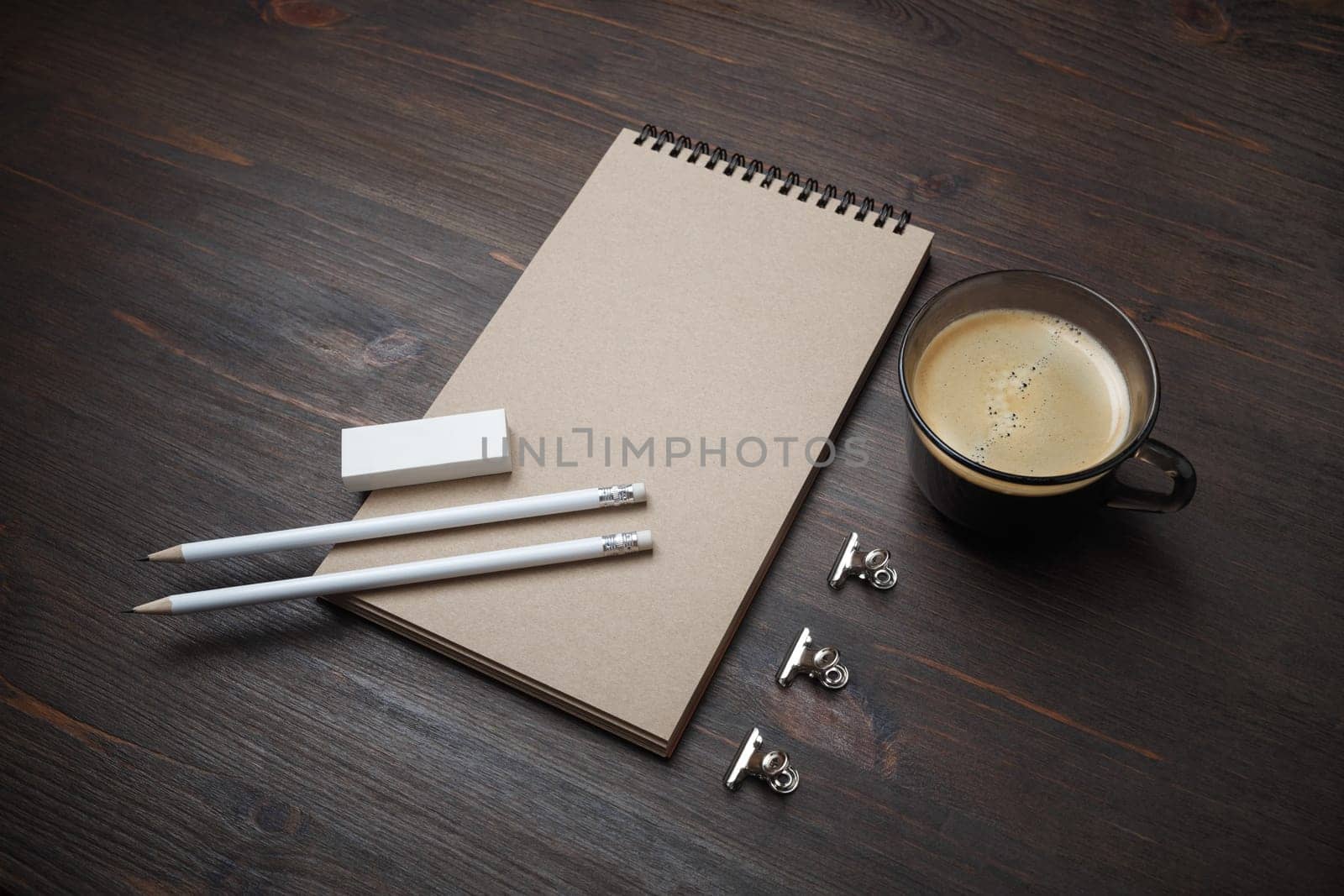 Blank kraft notepad, pencils, eraser and coffee cup on wooden background. Responsive design mockup.