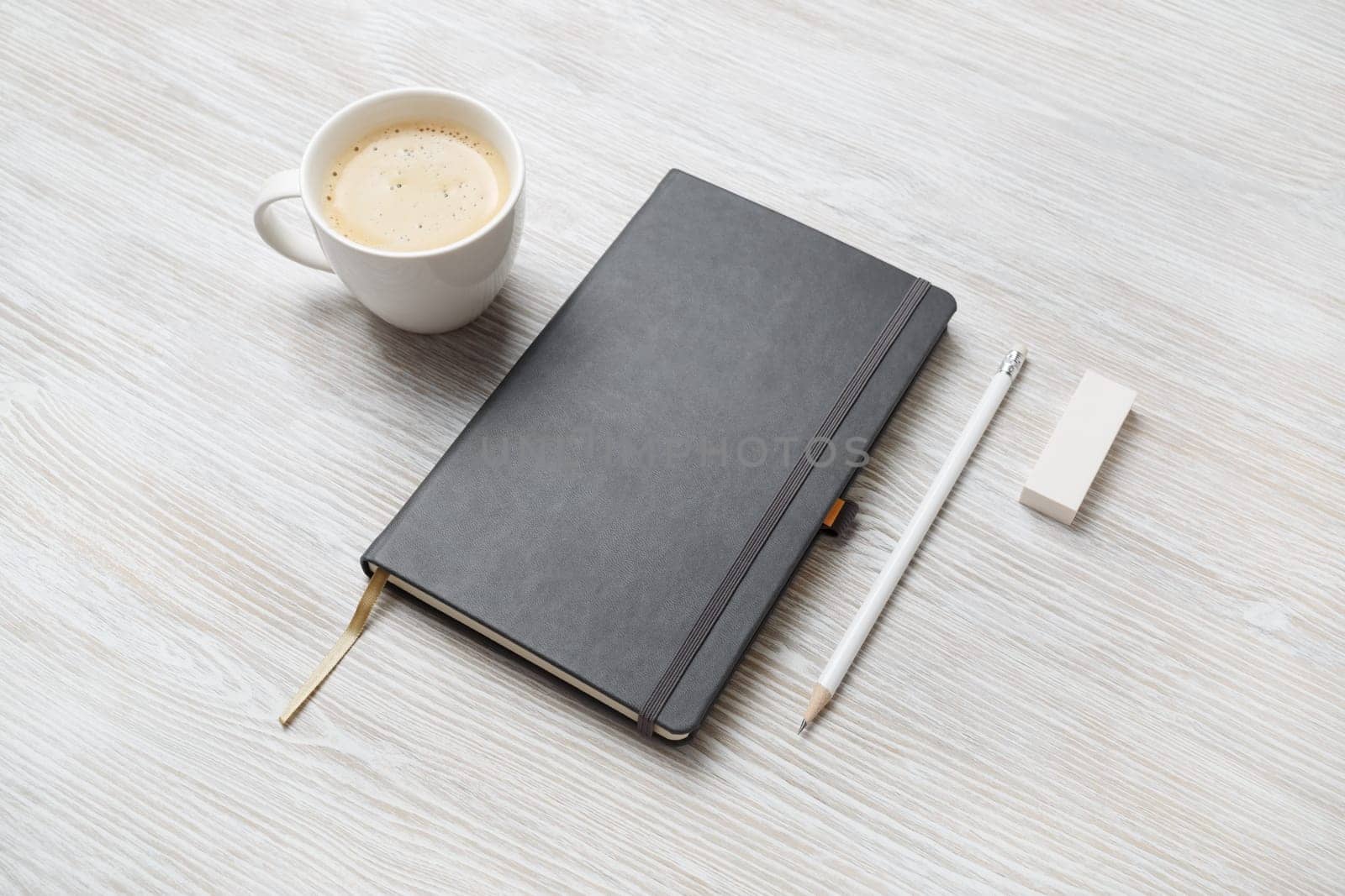 Photo of blank closed notepad, pencil, eraser and coffee cup on light wooden background. Responsive design mockup. Stationery elements. Template for placing your design.