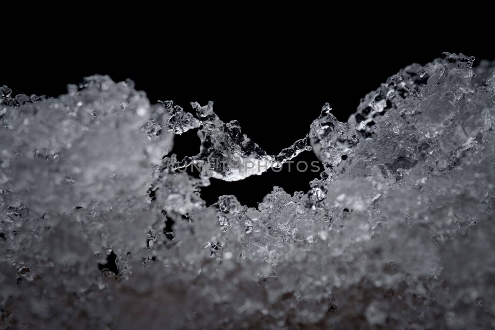 Super close up abstract image of slowly thawing snow. Minute detail of the ice crystals are visible, plain black background. Cold outdoor weather