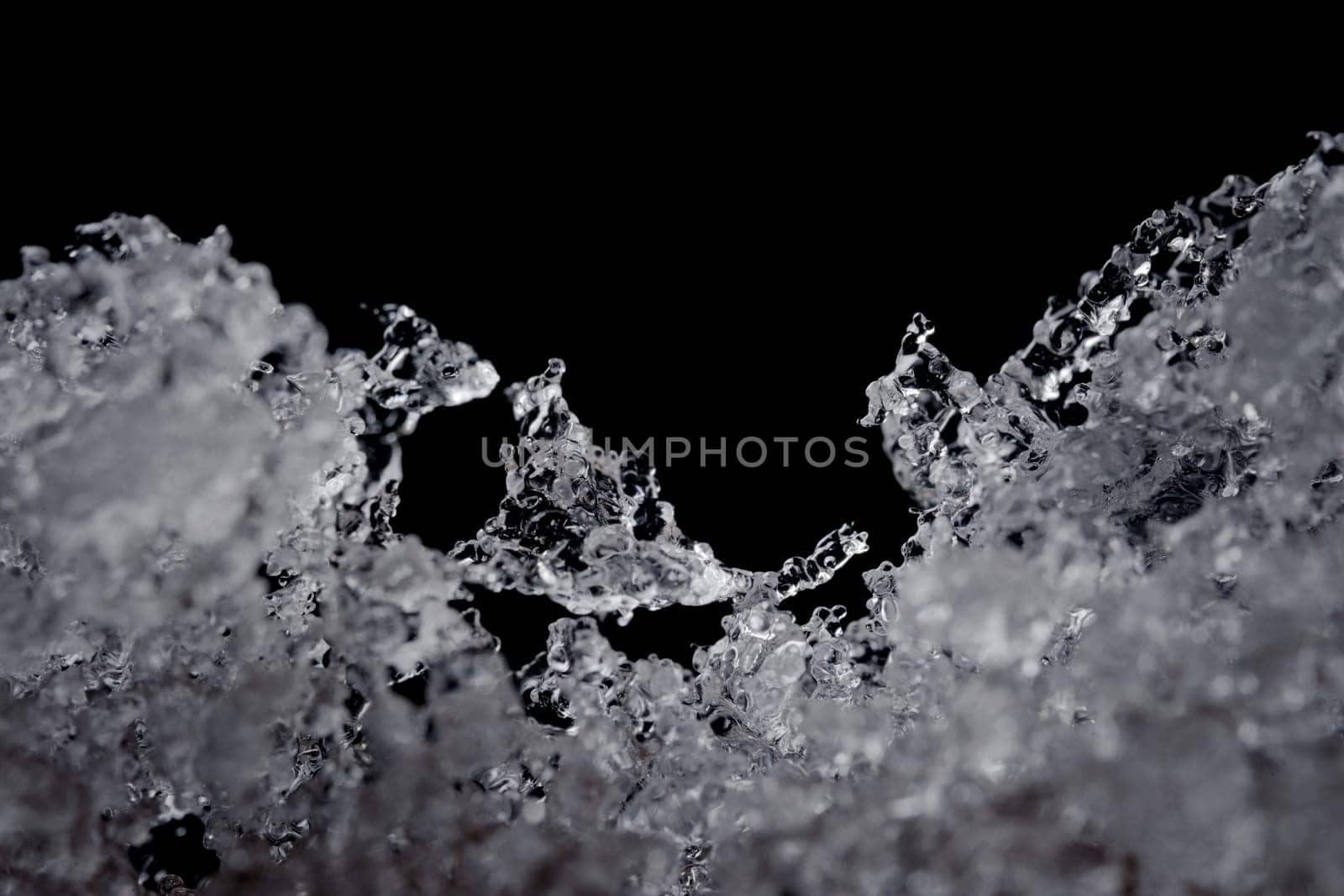 Intricate details of melting water particles. Focus on odd shaped ice crystal in the middle, but plain black background with copy space above.