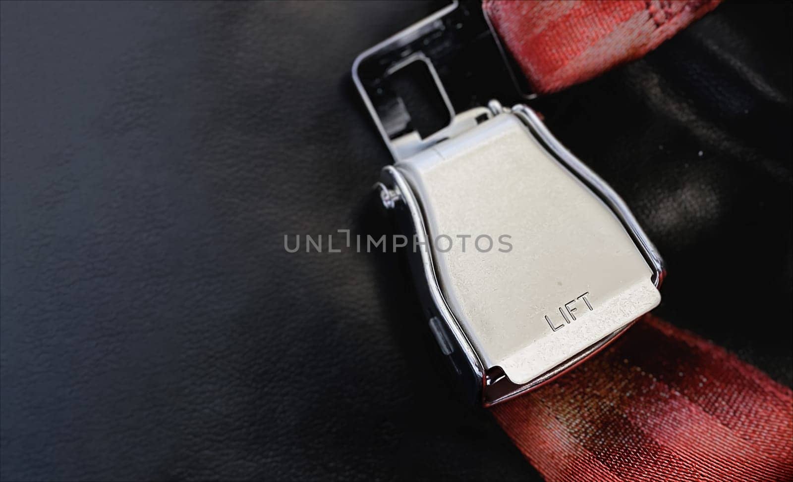 Red lap belt of an empty seat inside an airplane with the word LIFT embossed on the metal. Safe travel