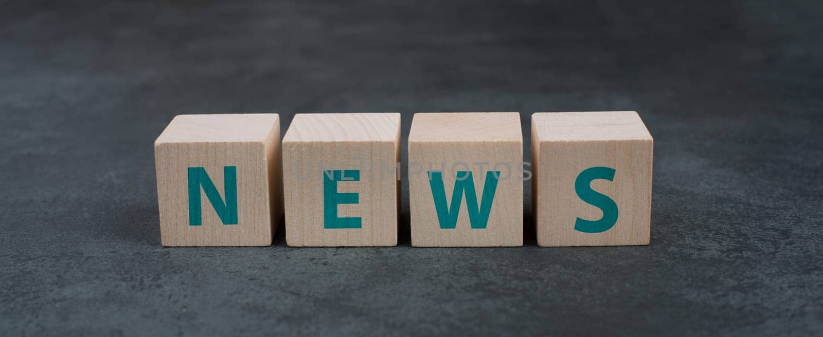 The word news is standing on wooden blocks, dark background