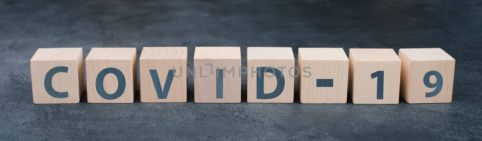 The word covid-19 is standing on wooden blocks, dark background, headline