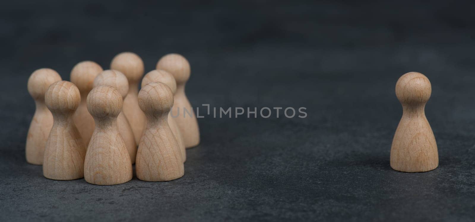 Group of wooden figures standing together, one leader standing alone on the opposite side
