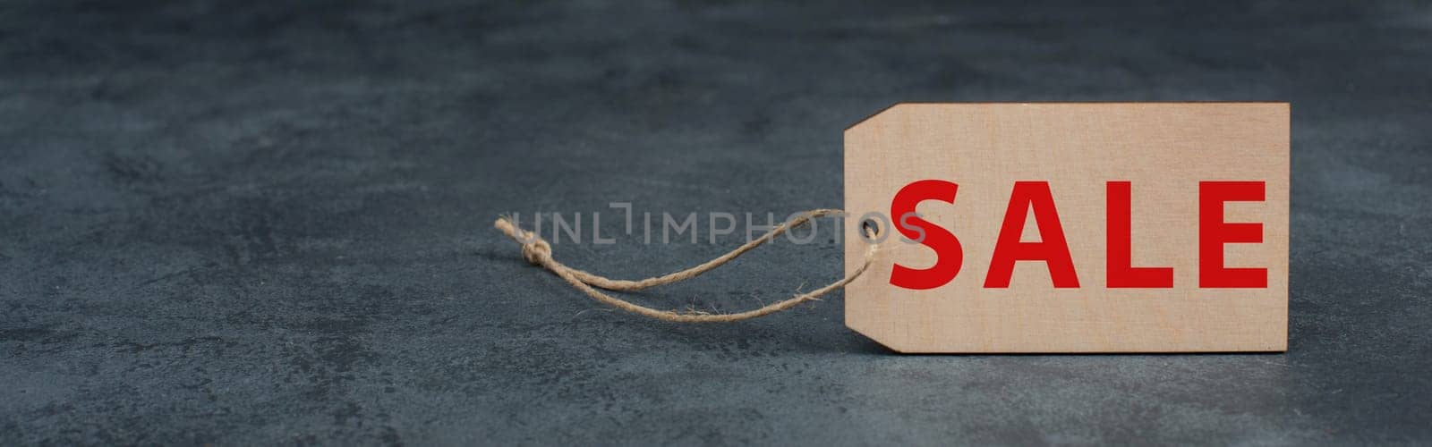Wooden label with the word sale in red color, dark textured background, empty copy space