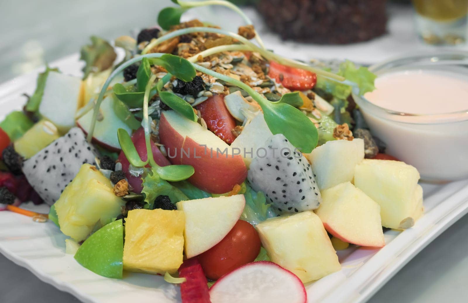 Vegetable and fruit salad with dressings on white plate. Pineapple, lettuce, apple, cucumber, carrot, dragon fruit, kiwifruit, radish, tomato, sprouts, seeds and nuts. Healthy vegan and diet food concept.