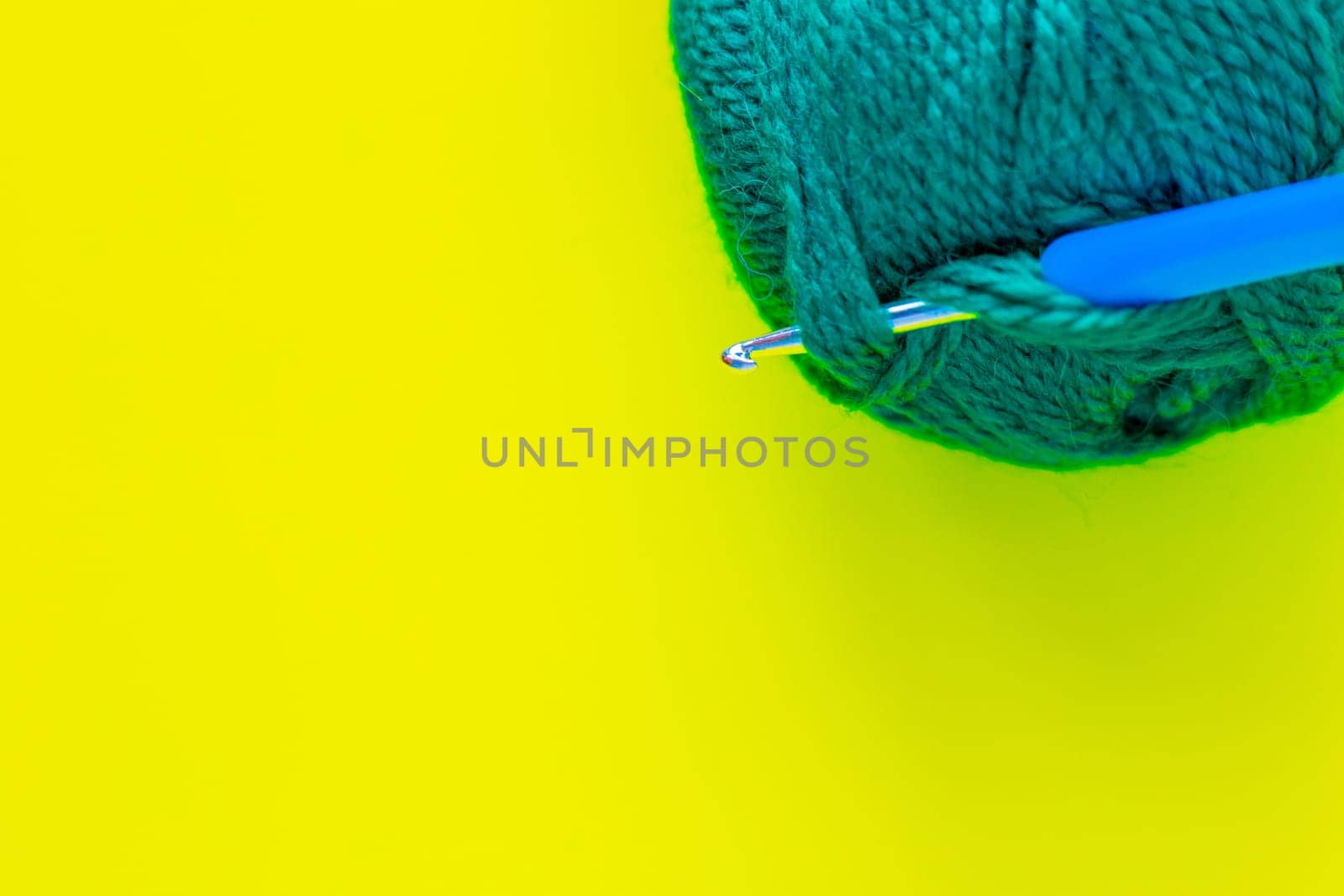 A metal hook with a blue handle is inserted into a skein of green yarn in the upper corner of the photo on a yellow background. top view, flat lay, copy space, isolate. High quality photo