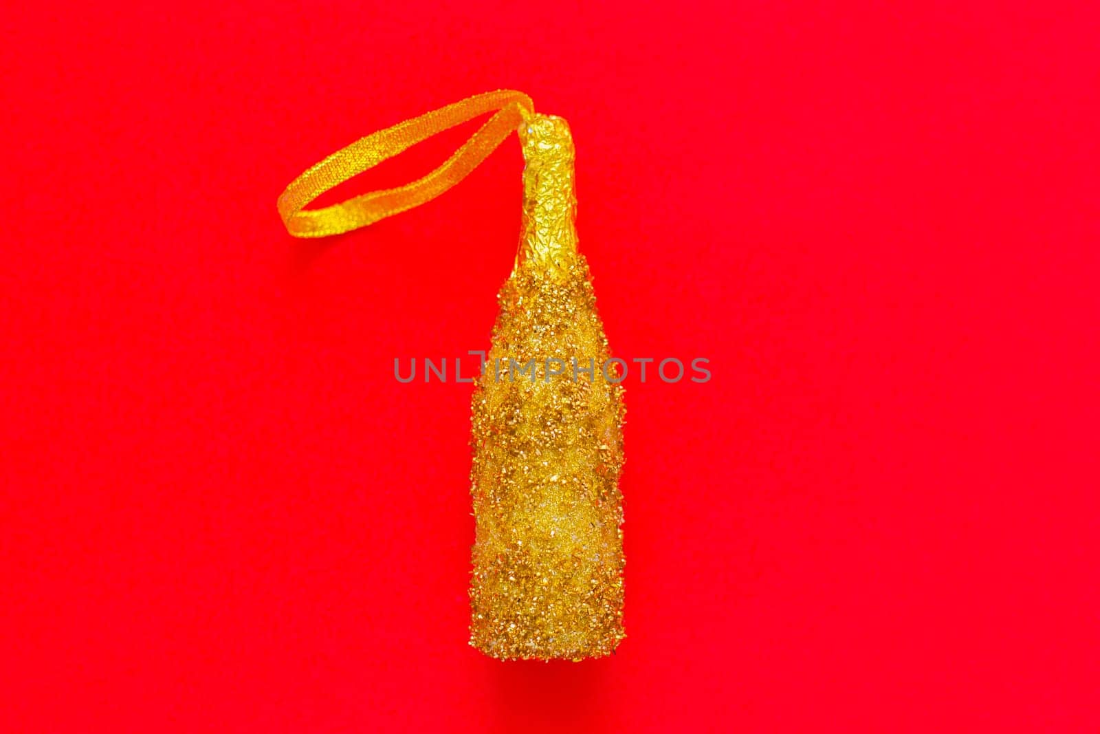 A toy for the Christmas tree in the form of a golden champagne bottle with sequins lies in the center on a red background. top view, flat lay, copy space, isolate. High quality photo