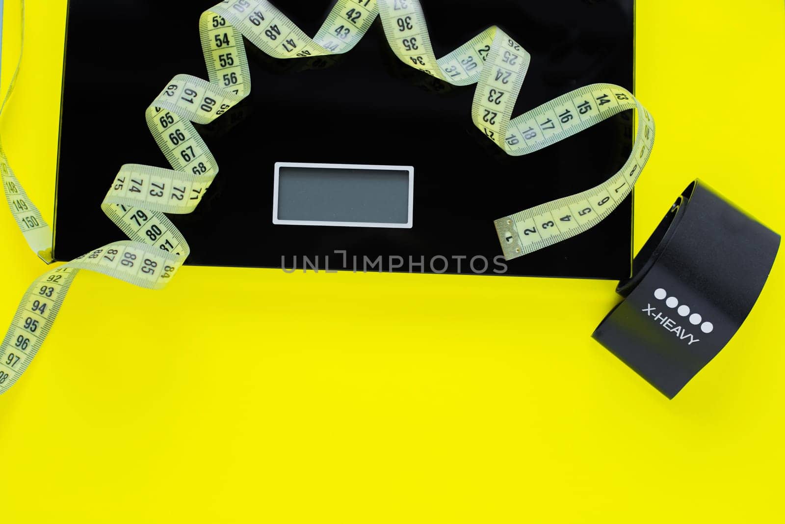 A weight scale, a black fitness tape and a yellow measuring tape lie on a yellow background on top of the photo. top view, flat lay, copy space, isolate. High quality photo