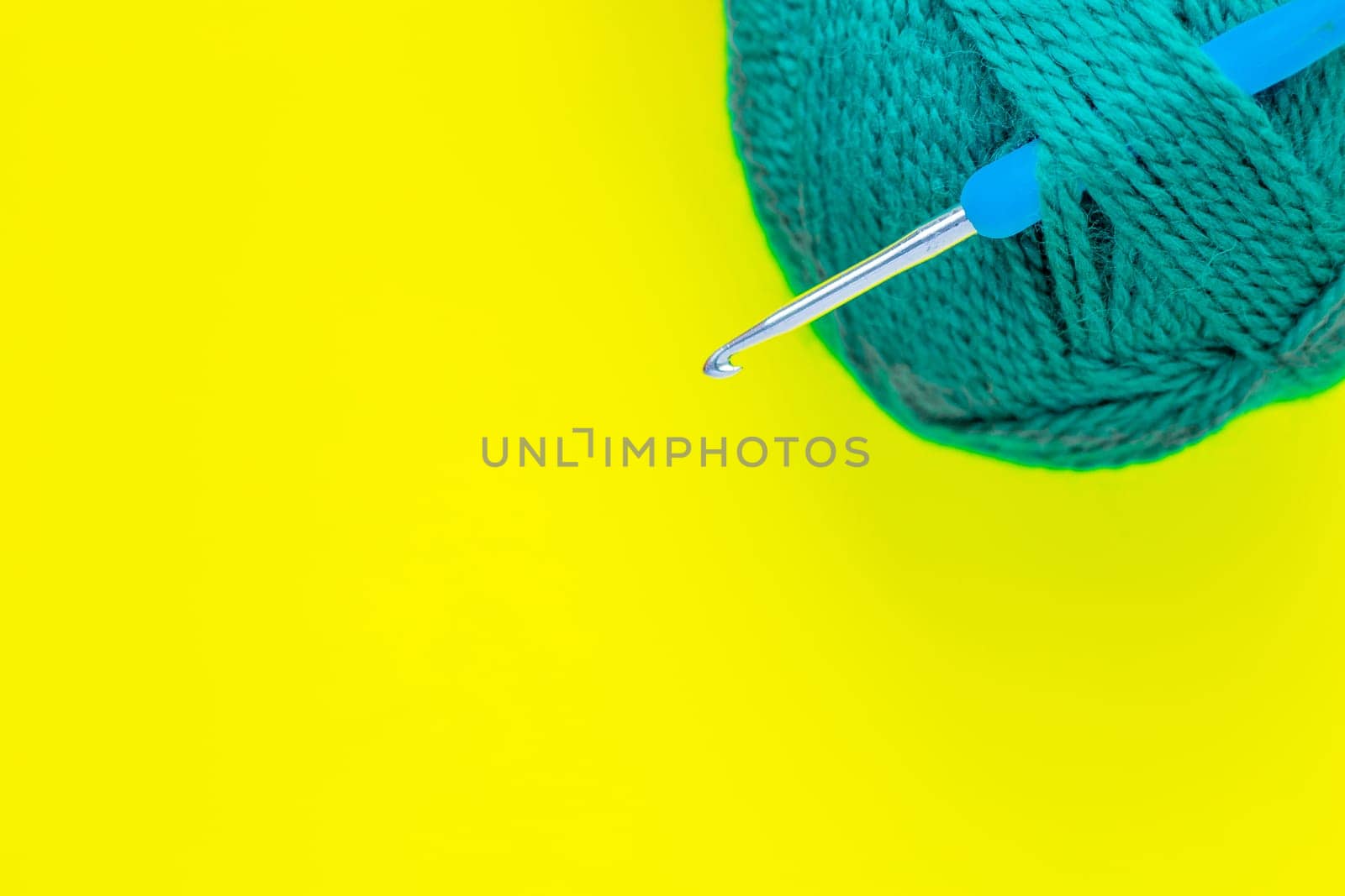 A metal hook with a blue handle is inserted into a skein of green yarn in the upper corner of the photo on a yellow background. top view, flat lay, copy space, isolate. High quality photo