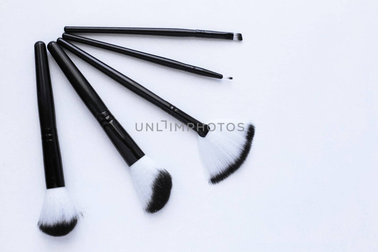 Black brushes with white and black pile for makeup of different sizes lie on a white background, they lie like a fan in the corner. top view, flat lay, copy space, isolate. High quality photo