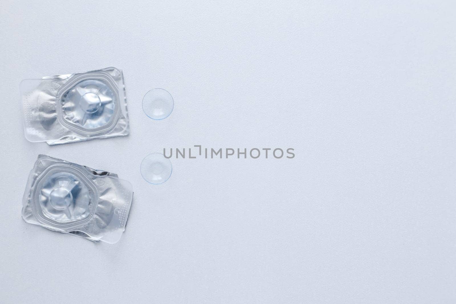 Two contact lenses in a closed package and two open contact lenses lie on the side on a white background with space for text. top view, flat lay, copy space, isolate. High quality photo