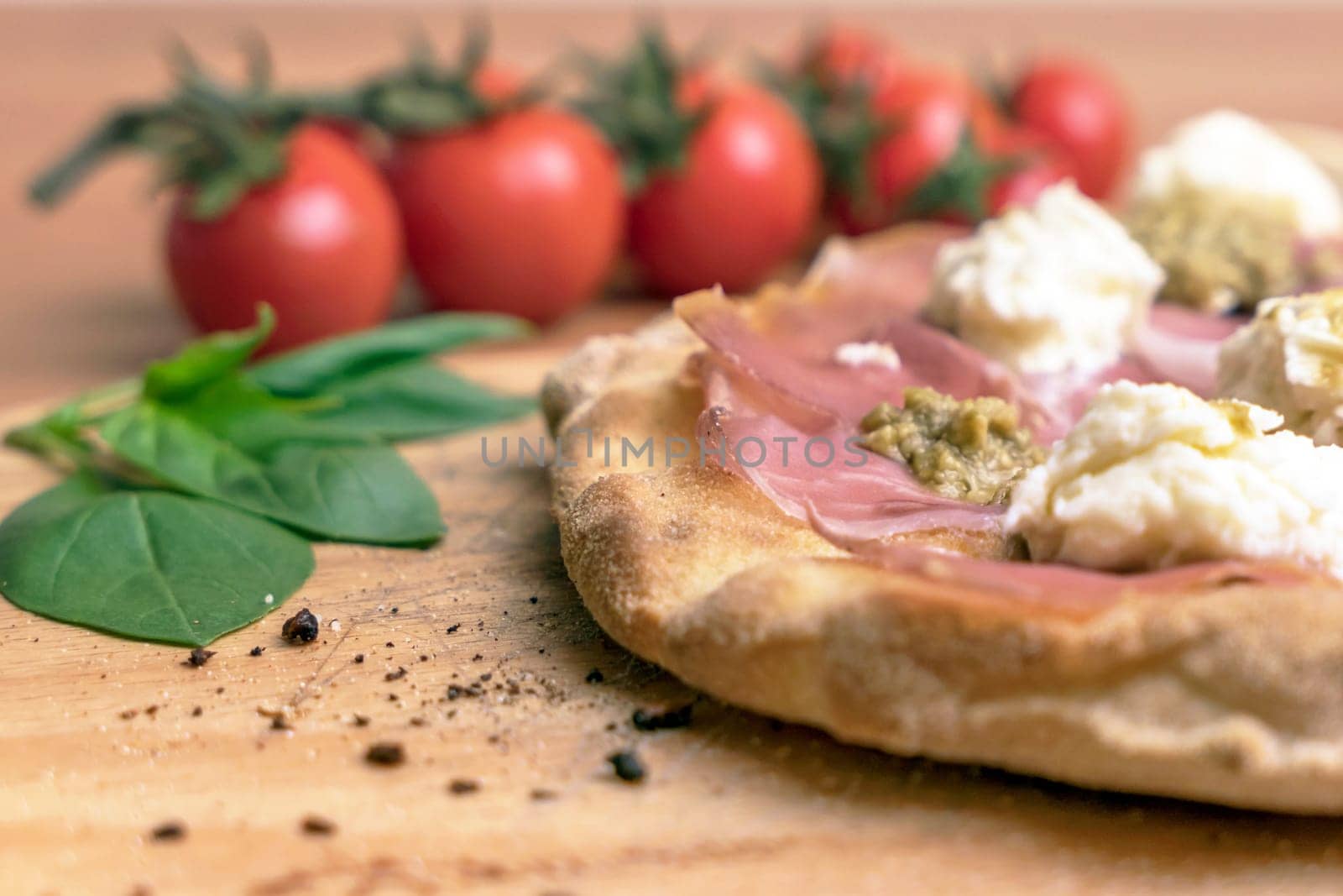 Close up of italian pizza on a wooden cutting board. On background defocused tomatoes and basil.