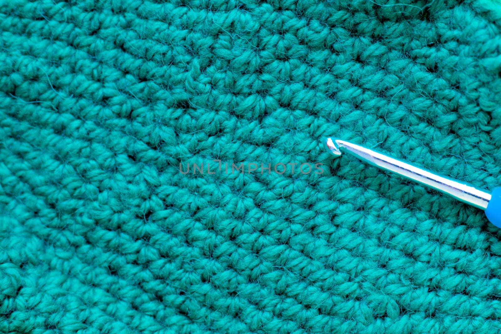 A metal hook with a blue handle lies on a knitted fragment of green color. High quality photo