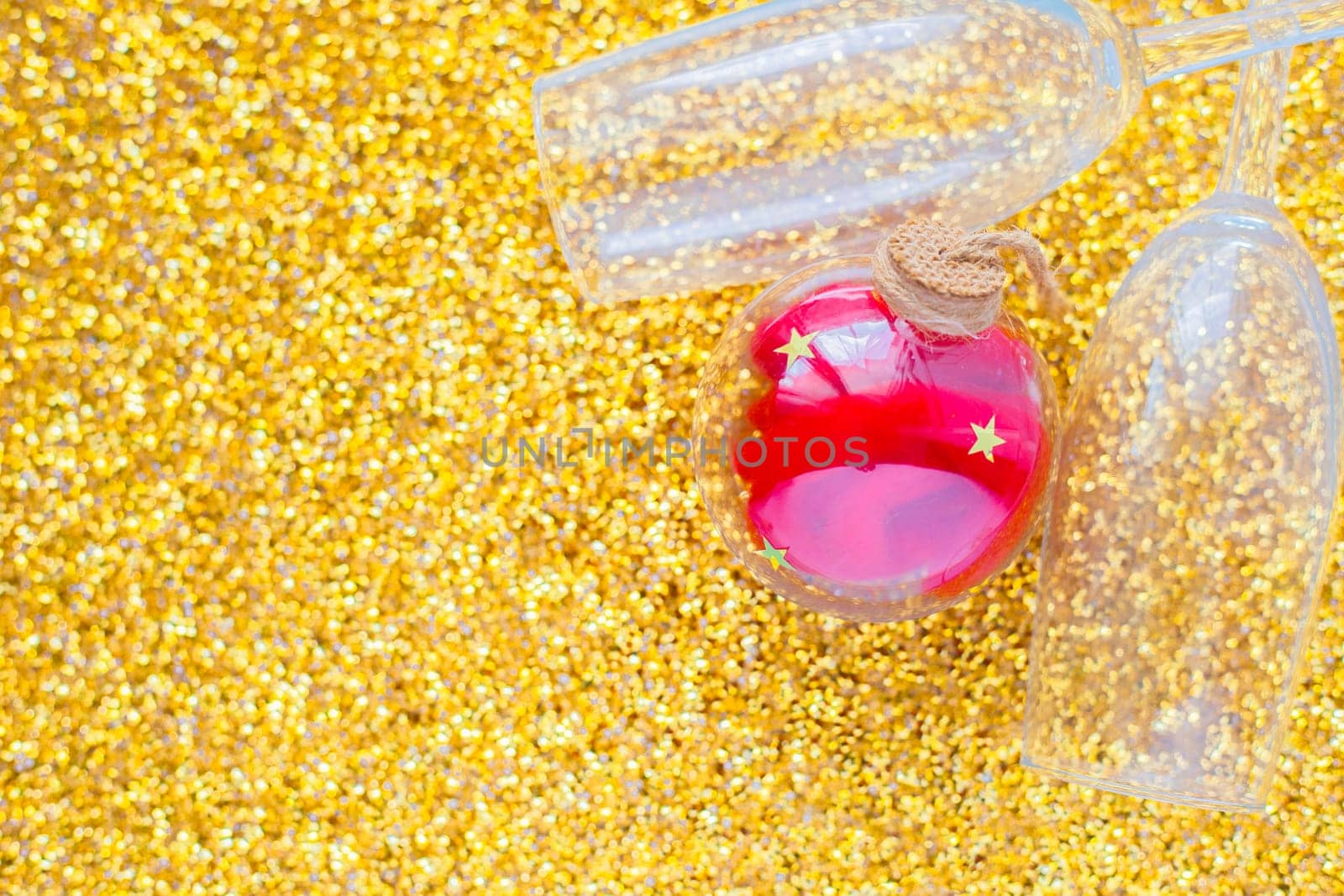 Two champagne glasses are lying in the corner of the picture, between them is a red Christmas ball on a gold textured background. top view, flat lay, copy space, isolate. High quality photo