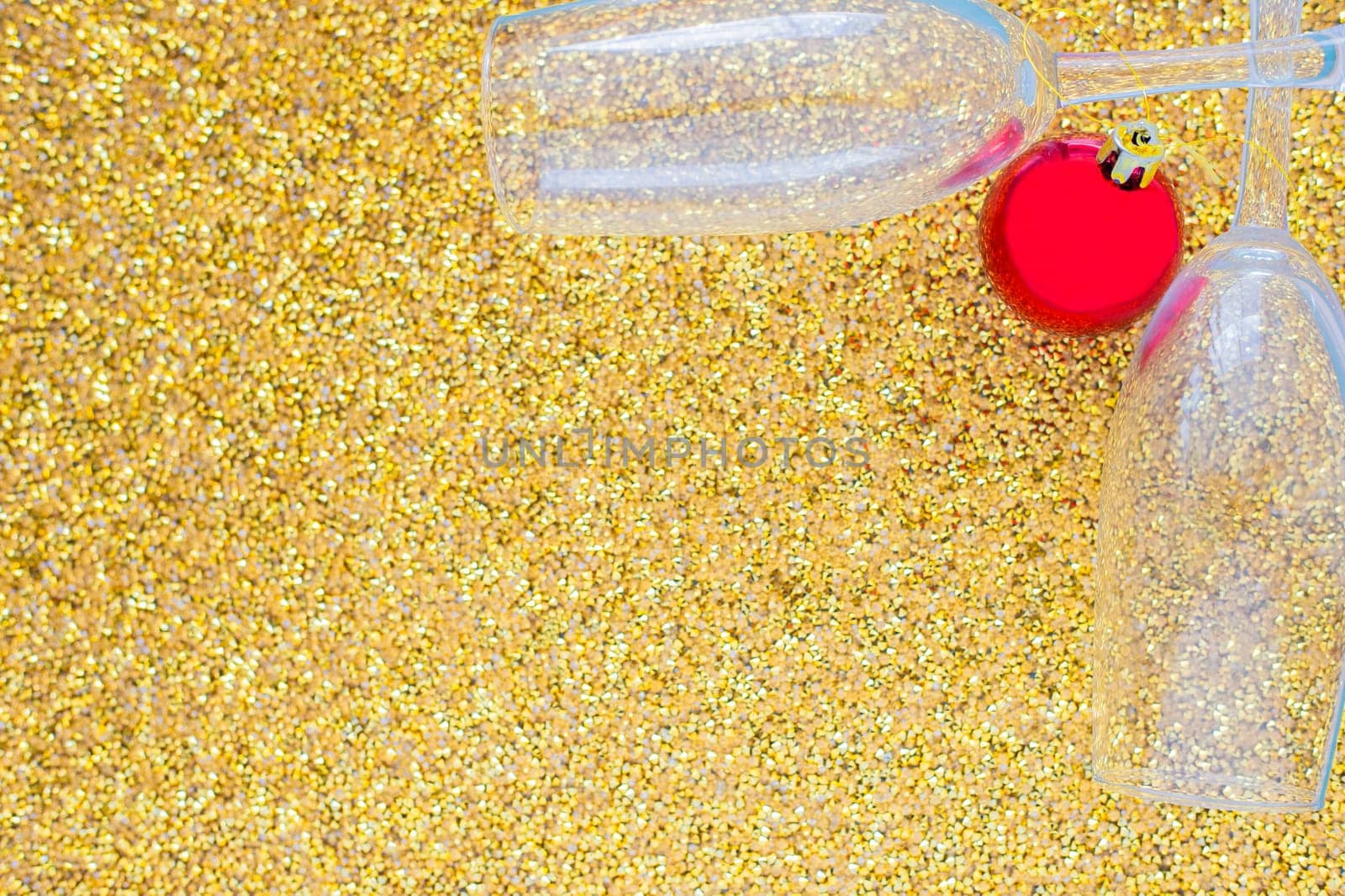 Two champagne glasses are lying in the corner of the picture, between them is a red Christmas ball on a gold textured background. top view, flat lay, copy space, isolate. High quality photo