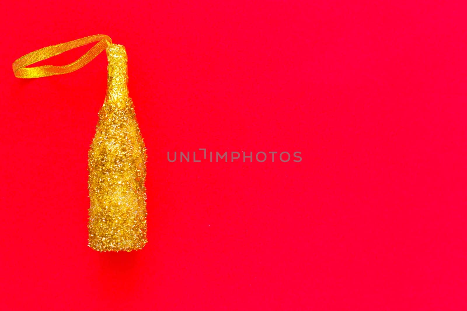 A toy for the Christmas tree in the form of a golden champagne bottle with sequins lies on the side on a red background. top view, flat lay, copy space, isolate. High quality photo