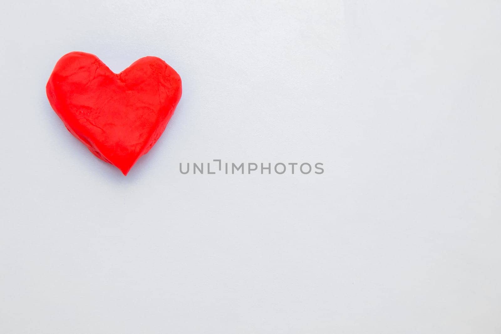 A heart made of red dough for modeling lies on the side of the photo. High quality photo
