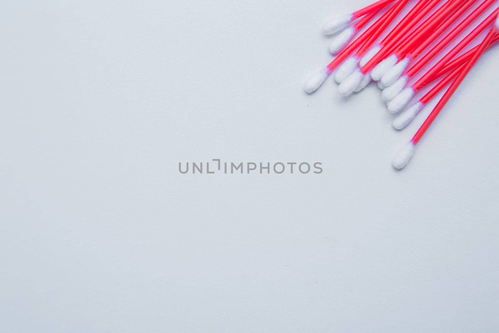 Disposable ear sticks with a red wand are lying on a white background in the upper corner. top view, flat lay, copy space, isolate. High quality photo