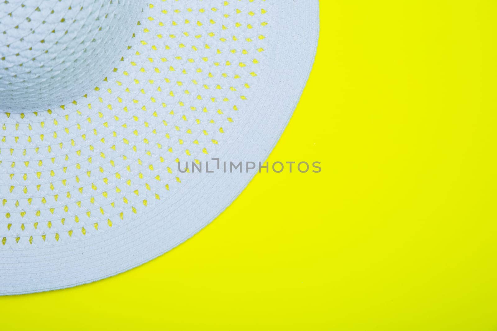 A white sun hat with a wide brim lies on a yellow background with a place for text. High quality photo