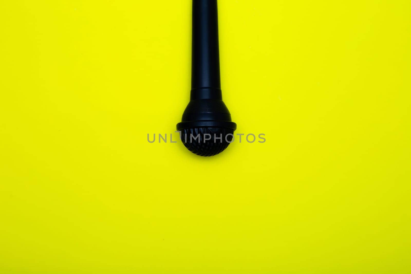 A black microphone hangs from above on a yellow background. High quality photo