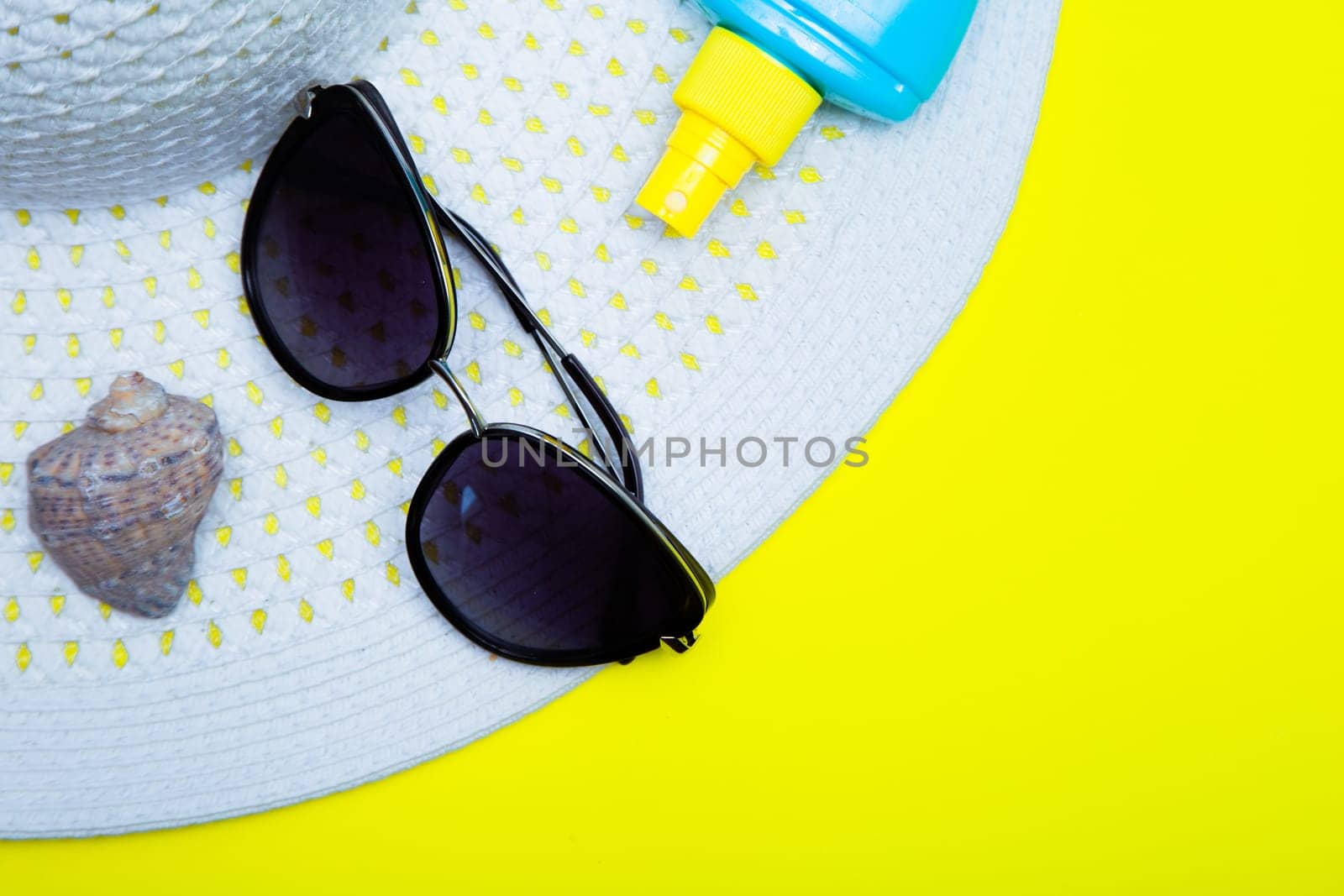 On a white sun hat with a wide brim is a shell, sun glasses and suntan on a yellow background with a place for text. High quality photo
