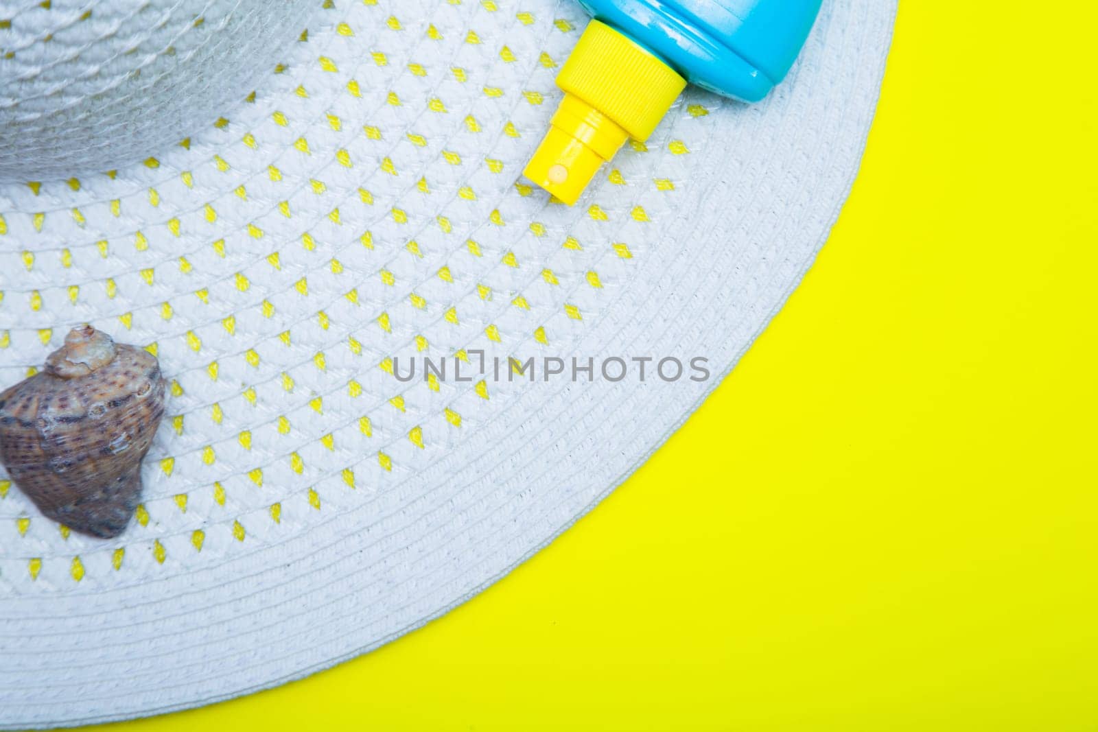 On a white sun hat with a wide brim there is a shell and a tanning agent on a yellow background with a place for text. High quality photo