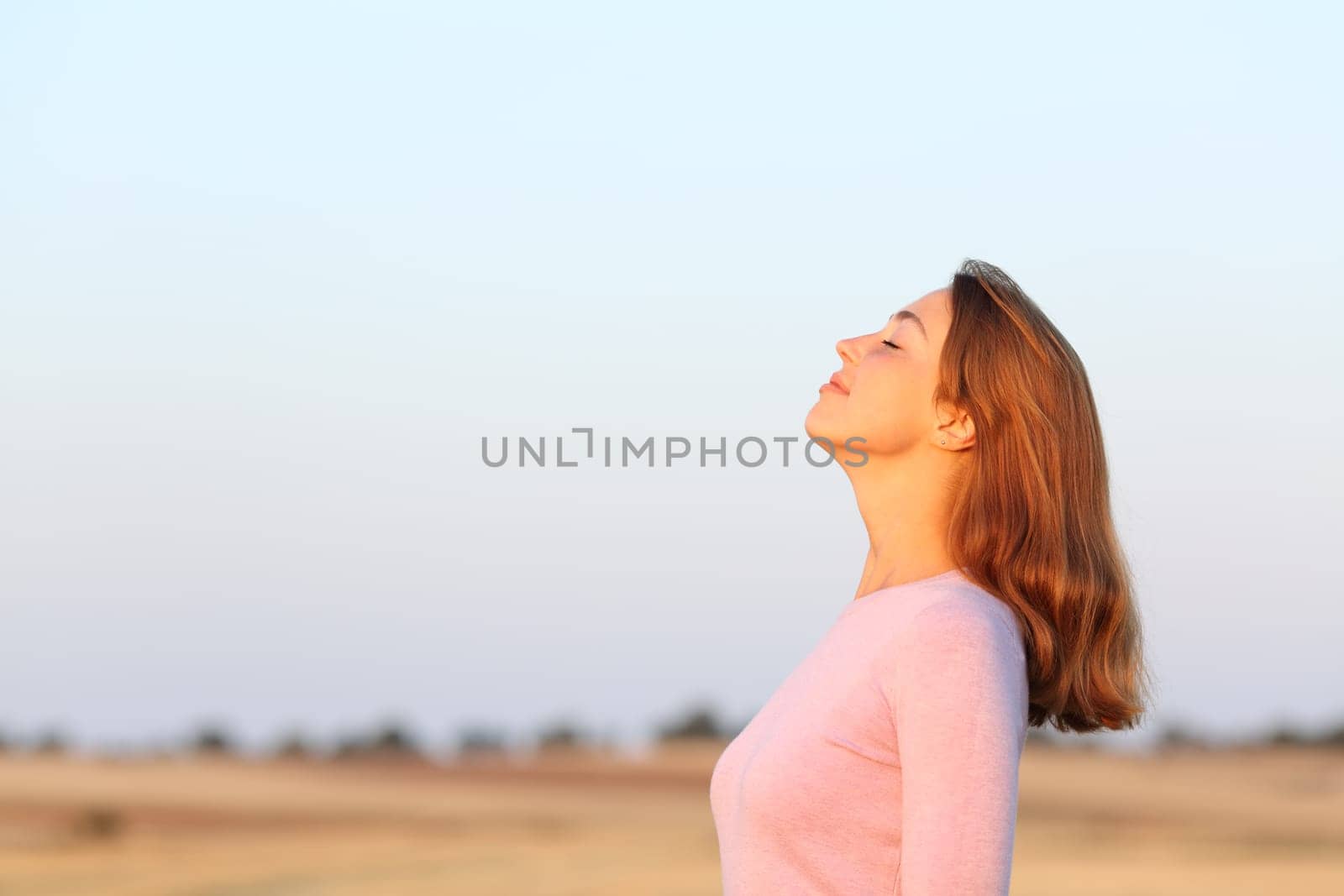 Side view portrait of a relaxed woman breathing fresh air at sunrise in a field