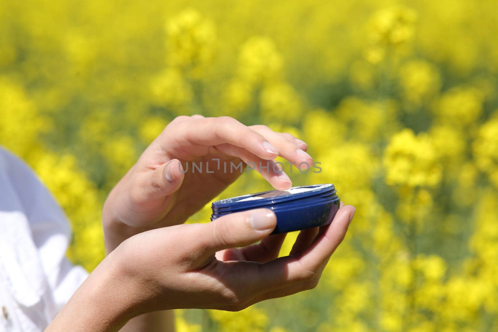 Close up of a woman hands holding moisturizer jar ready to apply in a yellow field